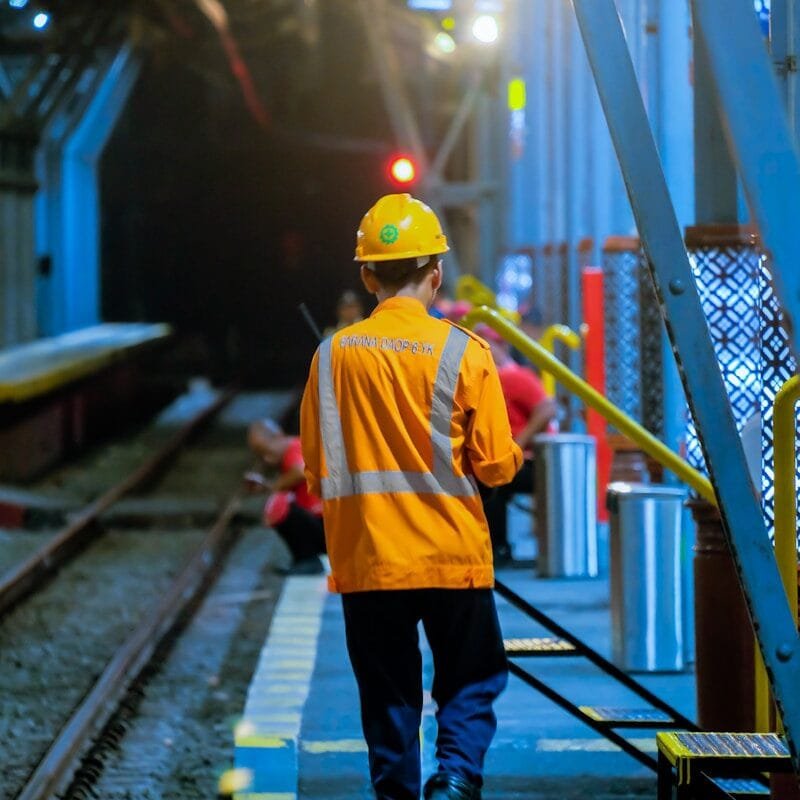 a man in a yellow jacket is walking down a train track